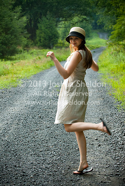 Young woman kicking up her heels on gravel country road