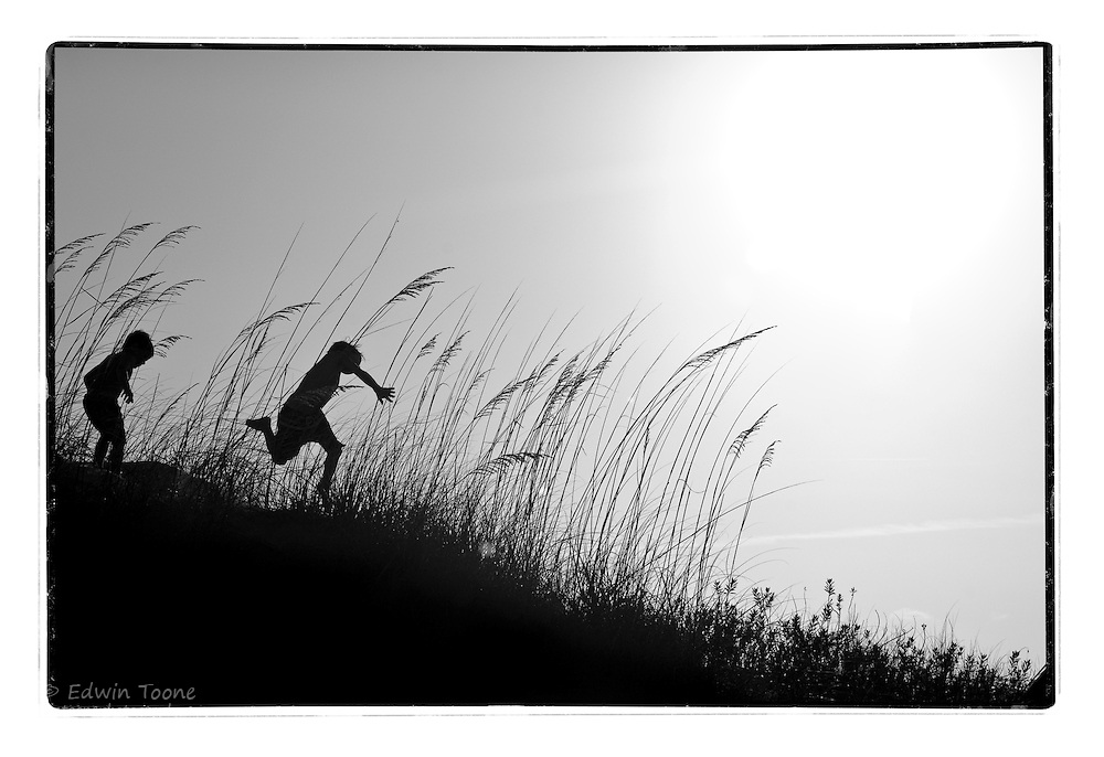 The silhouette of 2 boys as they jump through the sand dunes on Lee's Island, North Carolina.