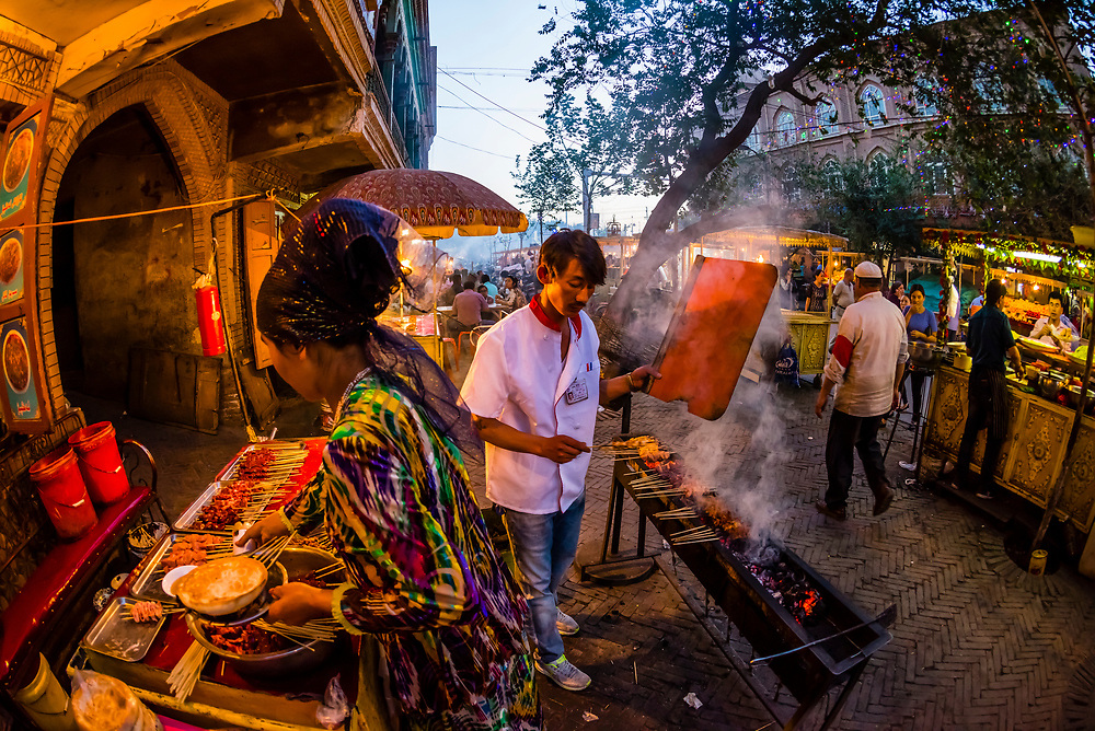 Street vendors cooking kebabs in the night market in the bazaar in Kashgar an oasis city in Xinjiang Province, China. It is the westernmost city in China, located near the border with Afghanistan, Kyrgyzstan, Pakistan, and Tajikistan. It was a stop on the Silk Road. Uyghur people are a Central Asian people of Muslim Turkic origin. They are China’s largest minority group.