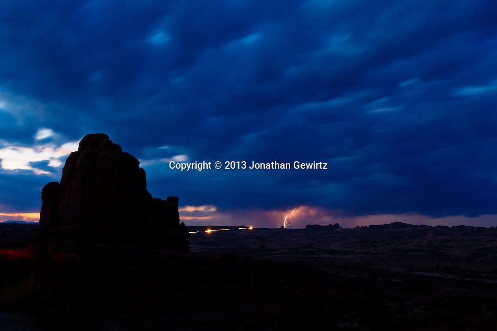 Lightning from a distant storm and headlights on the main park road illuminate rock formations in this long-exposure view of Arches National Park, Utah. WATERMARKS WILL NOT APPEAR ON PRINTS OR LICENSED IMAGES.