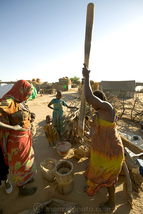 The Breidjing Refugee Camp, Eastern Chad on the Sudanese border shelters 30,000 people who have fled their homes in Darfur, Sudan. Food is distributed free of charge by the United Nations WFP (World Food Program). Here, women pound grain into meal with a traditional heavy wooden mortar and pestle. (Supporting image from the project Hungry Planet: What the World Eats.)