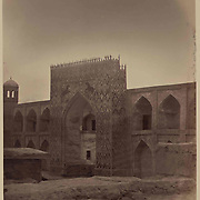 1865<br />
This photograph of the Rustem-Bek Madrasah in Ura-Tyube (present-day Istarawshan, Tajikistan) is from the archeological part of Turkestan Album. The six-volume photographic survey was produced in 1871–72 under the patronage of General Konstantin P. von Kaufman, the first governor-general (1867–82) of Turkestan, as the Russian Empire’s Central Asian territories were called. Ura-Tyube (in Tajik, Ura-Teppa) is one of the oldest settlements in Central Asia. Located near the Syr Darya River some 80 kilometers southwest of Khujand, Ura-Tyube flourished under the Samanid dynasty in the 10th-11th centuries. Like many towns in the area, it was sacked by the Mongols in the early 13th century. It revived under the Timurids in the late 14th and 15th centuries and submitted to the Bukhara Shaybanids in the 16th century. In the late 18th century it achieved autonomy before becoming part of the Khanate of Kokand. Ura-Tyube was taken by the Russians in October 1866. Among its religious institutions was the madrasah, which is shown here. The two-storied structure follows a 16th-century design, with arched cells for living and study and a large interior courtyard. The main entrance has an iwan (vaulted hall, walled on three sides, with one end open) arch, and the facade is flanked by corner towers. The iwan facade is covered by a surfeit of crude decorative work that appears to be later than the original structure—perhaps as late as the 19th century.