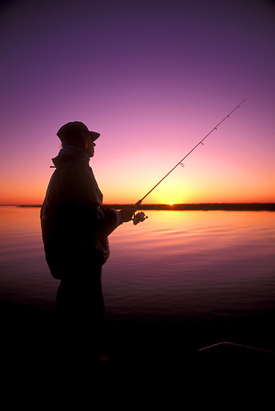 Stock photo of the silhouette of a man fishing in the bay at sunset