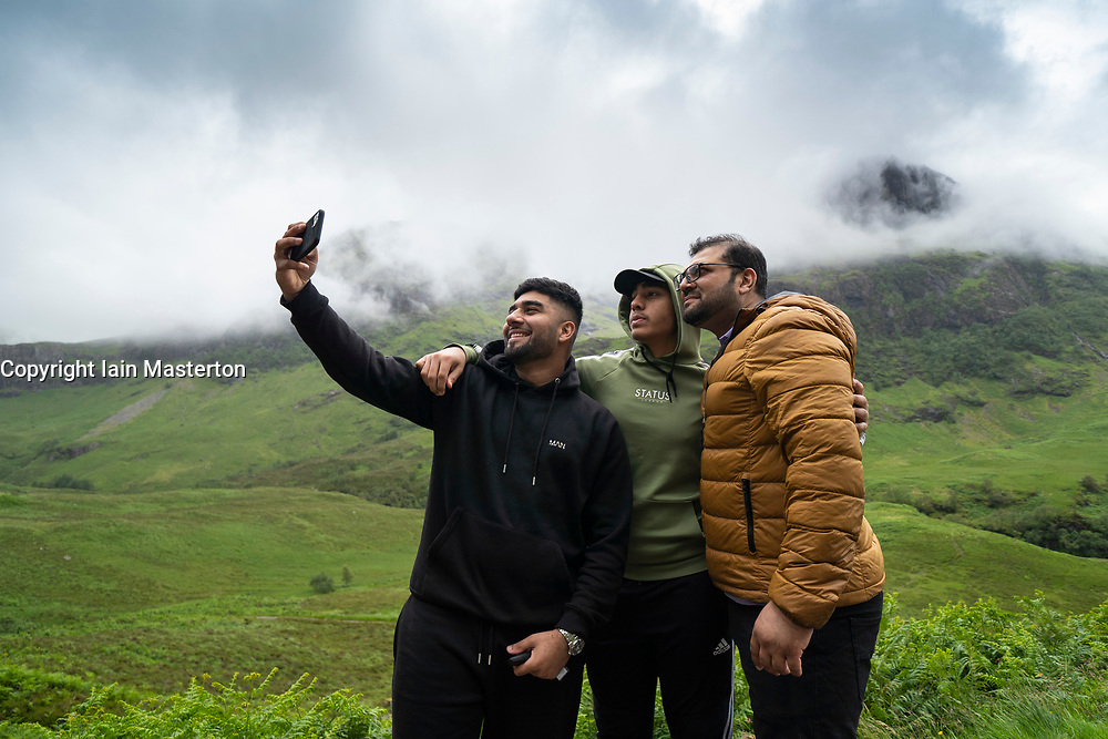 Glen Coe, Scotland, UK. 4 July, 2020. Tourists travel to Glen Coe on first weekend after 5 mile travel restriction was lifted by the Scottish Government. Pictured; cIndian day-trippers take selfie photograph with spectacular mountain backdrop in Glen Coe. Iain Masterton/Alamy Live News