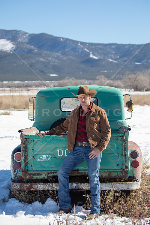 hot rugged cowboy leaning against a rustic truck in the snow