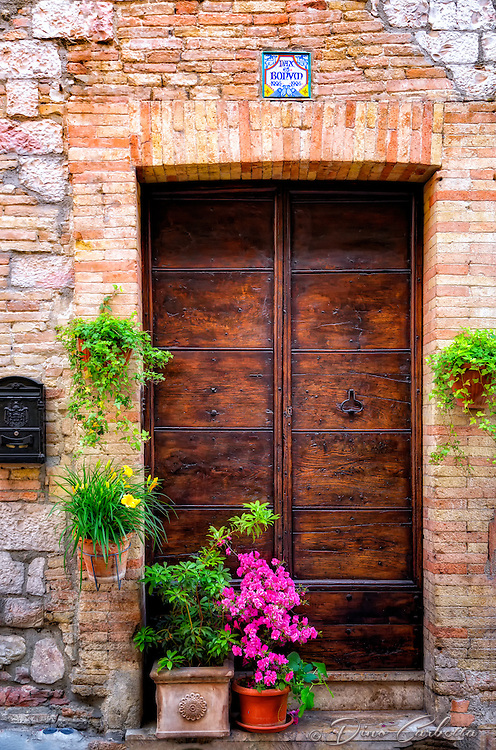 “Beautiful flowers and Pax et bonum adorn the doors of Assisi”…<br />
<br />
Italy is famous for its display of fresh and beautiful flowers and foliage outside the windows and doors throughout the countryside, and Assisi was no different with the exception of the perfection of their presentation. I am sure the Chamber of Commerce in Assisi is quite busy maintaining the continuity and beauty of Assisi, but perhaps there is no need as the residents all seem perfectly happy to respect and display all its beauty. The streets, walkways, and general environment were the most immaculate of any town I witnessed in Italy, and the most religious of anyplace on my journey. The town became a mystic and peaceful shrine in the early darkness of night after all the tourists departed, and all the prayers offered that day reflected and echoed off the ancient walls. Even the vending machines contained Rosaries, and its residents strolled about dressed in their religious attire with permanent smiles upon their faces. I am sure there are many remarkable religious destinations in the world, but in this photographer’s opinion…Assisi has no spiritual equal on this earth. Pax et bonum (peace and the good, the motto of St Francis), is displayed above all doors and virtually everywhere in Assisi. Many in passing just offer a greeting with a friendly “Pax”, or Peace!